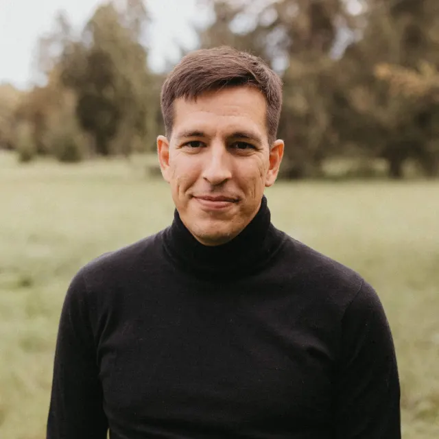 Rasmus in a black turtleneck, smiling in a green meadow